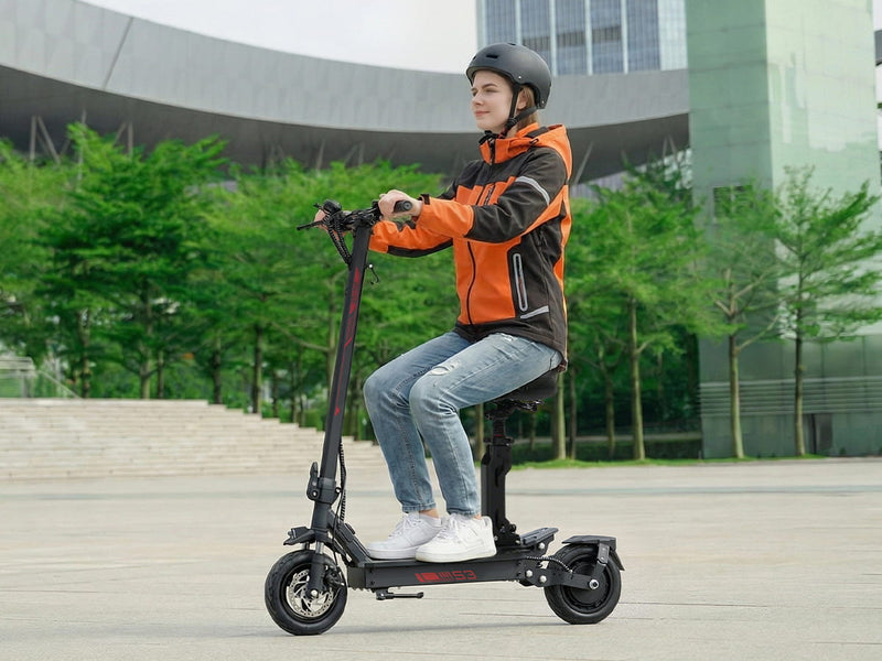 Person riding an electric scooter outdoors with greenery and a building in the background